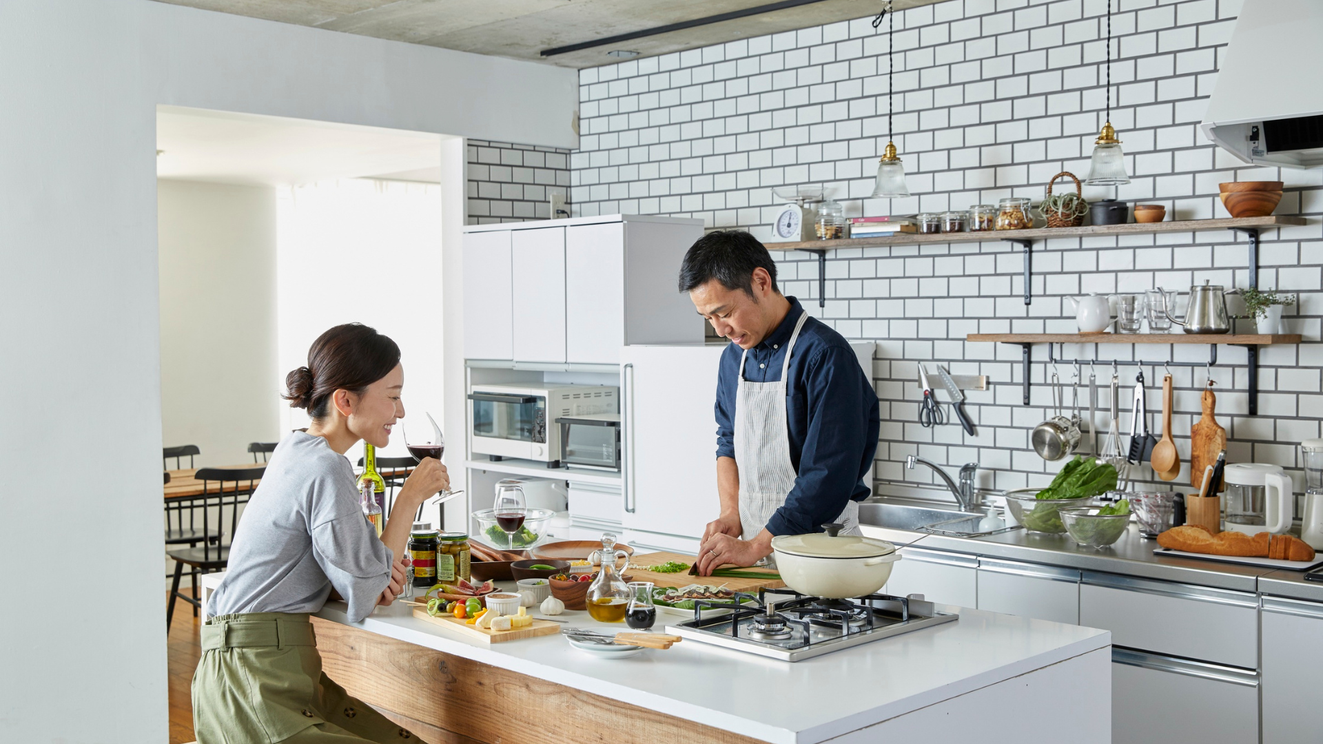 Couple cooking together in a modern kitchen with white subway tile backsplash and open shelving.